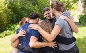 Corporate team spending weekend together outdoors. Men and women in casual forming circle and hugging in park. Corporate teambuilding concept